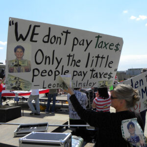 woman holding a large sign taking up much of the frame with a few others standing nearby