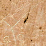 pertoglyh on stone with images of "stick" people facing two paths- one with a locomotive running away (representing modern technology) and another path that includes farming corn and living close to the earth