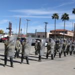 a line of military police with riot shields practicing a formation in a parking lot