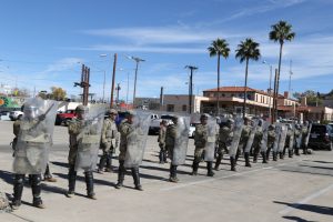 a line of military police with riot shields practicing a formation in a parking lot