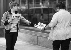 activist hands a War Resisters League federal budget pie chart to a passer-by