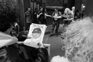 person holds War Resisters League federal budget pie chart in foreground while redirection ceremony is taking place in the background