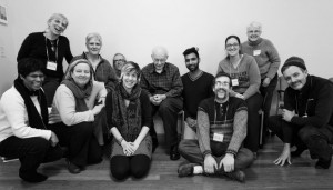 black and white photo of about a dozen people sitting on chair and floor, smiling for the camera