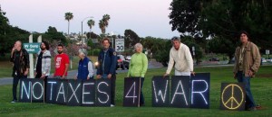 eight people pose behind signs reading "no taxes 4 war"