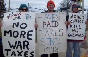 3 people holding signs stating opposition to paying taxes for war