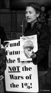 woman holding a sign that reads "Funding the future of the 99% NOT the wars of the 1%