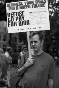 Walter Goodman holding a sign on a stick: "Redirect Your Taxes for a Green Future. Refuse to Pay for War."